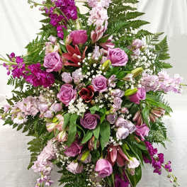 Tall cascading arrangement of purple roses, pink lilies, and white filler flowers in an oval spray shape.
