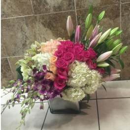 Mixed bouquet with pink roses, lilies, and white hydrangeas in a square vase