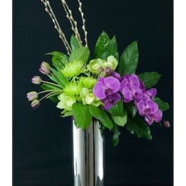 Purple orchids and green flowers in a tall silver vase