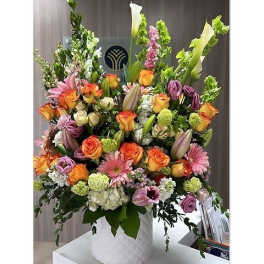 Tall mixed bouquet in a white textured vase with orange, pink, and purple flowers