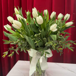 White tulips arranged in a clear glass vase with a white ribbon