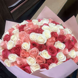Large bouquet of pink, red, and white roses wrapped in pale pink paper