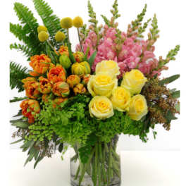 Mixed bouquet of yellow roses, pink snapdragons, and orange tulips in a glass vase