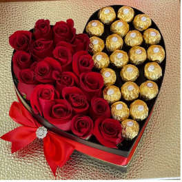 Heart-shaped box filled with red roses and gold-wrapped chocolates with a red bow
