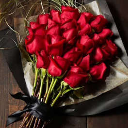 Bouquet of red roses wrapped in dark paper with a black ribbon