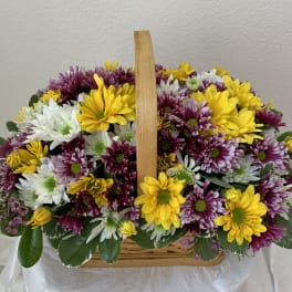 Basket of yellow, white, and purple daisy flowers with a wooden handle