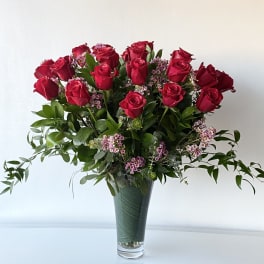 Red roses arranged in a tall glass vase with small pink filler flowers