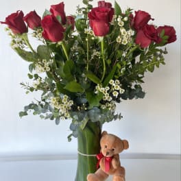 Red roses in a glass vase with a small teddy bear attached