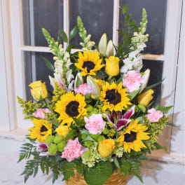 Basket arrangement with sunflowers, yellow roses, and pink carnations