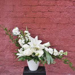 White floral arrangement in a white vase with lilies and roses
