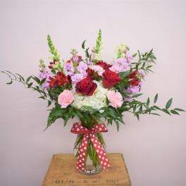 Mixed bouquet of red roses, pink carnations, and white hydrangeas in a glass vase