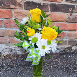 Yellow roses and white daisies in a glass vase with a duck ornament