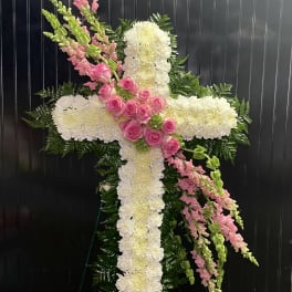 White floral cross with pink roses and snapdragons on a dark background