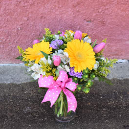 Bouquet of yellow daisies, pink tulips, and white flowers in a glass vase with a pink ribbon
