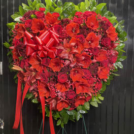 Heart-shaped red floral wreath with a ribbon bow on a stand