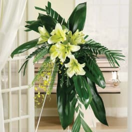 Standing floral spray with pale yellow lilies and tropical leaves