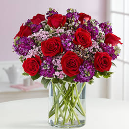 Bouquet of red roses and purple flowers in a clear glass vase