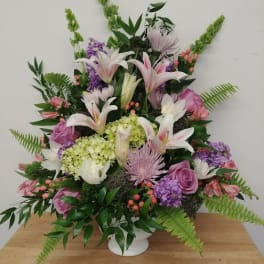 Large mixed floral arrangement in a white vase with lilies, roses, and purple blooms