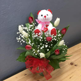 Bouquet of red and white tulips with a teddy bear and red ribbon in a glass vase