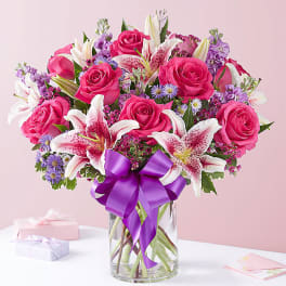 Pink roses and white lilies in a glass vase with a purple ribbon