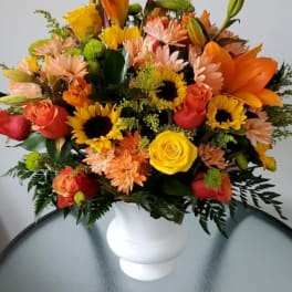 Mixed bouquet of orange, yellow, and pink flowers in a white vase