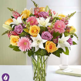 Mixed bouquet of roses, lilies, and pink daisies in a glass vase