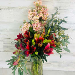 Tall bouquet of red lilies and pale pink flowers in a glass vase