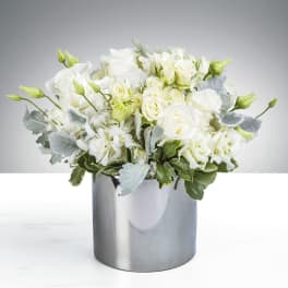 Low arrangement of white roses and hydrangeas in a shiny silver cylinder vase