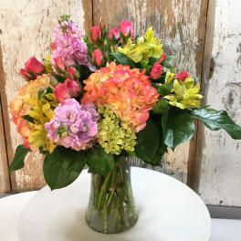 Mixed bouquet of pink, orange, and yellow flowers in a glass vase