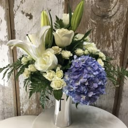 White lilies and roses with a blue hydrangea cluster in a silver vase.