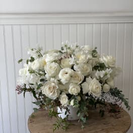White rose arrangement in a white vase with trailing greenery