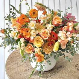 Colorful bouquet of orange, peach, and white flowers in a white vase