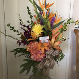 Tropical bouquet with orange bird-of-paradise and mixed blooms in a glass vase