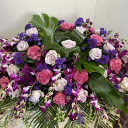 Large floral arrangement with pink roses, purple orchids, and broad tropical leaves