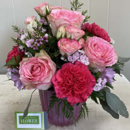 Pink roses, carnations, and daisies arranged in a pink glass vase