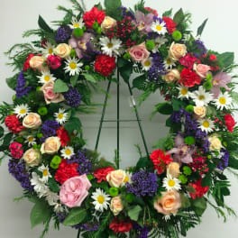 Large floral wreath on an easel with roses, daisies, and mixed blooms
