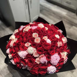 Large round bouquet of red and pink roses with pink peonies wrapped in black paper