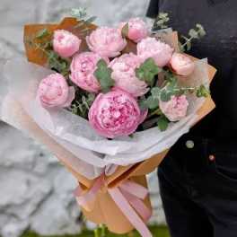 Bouquet of pink peonies wrapped in white and tan paper with a pink ribbon