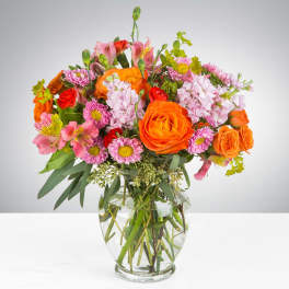 Bright bouquet of orange roses and pink mixed flowers in a clear glass vase
