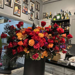 Large bouquet of red, orange, and pink roses in a black hatbox