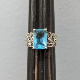 Silver ring with a rectangular blue gemstone on a dark stand