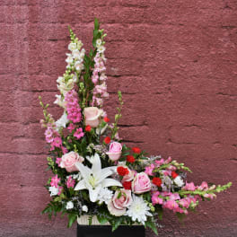 Tall pink and white floral arrangement with roses and lilies in a container