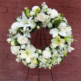 White floral wreath on a black stand with roses and lilies
