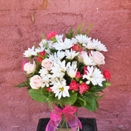 Bouquet of white daisies and pink roses in a glass vase with a pink ribbon