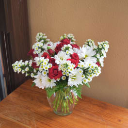 Red roses and white daisies arranged in a clear glass vase