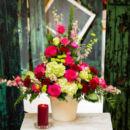 Tall mixed bouquet in a cream vase with a red candle beside it