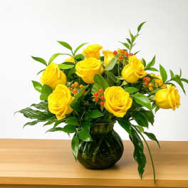Yellow roses arranged in a dark glass vase with green foliage
