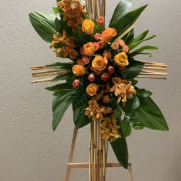 Orange roses and orchids arranged on a bamboo easel cross