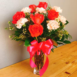 Red roses and pale pink carnations in a clear vase with a pink ribbon