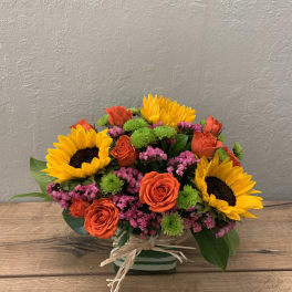 Bouquet of sunflowers, orange roses, and pink filler flowers in a striped vase